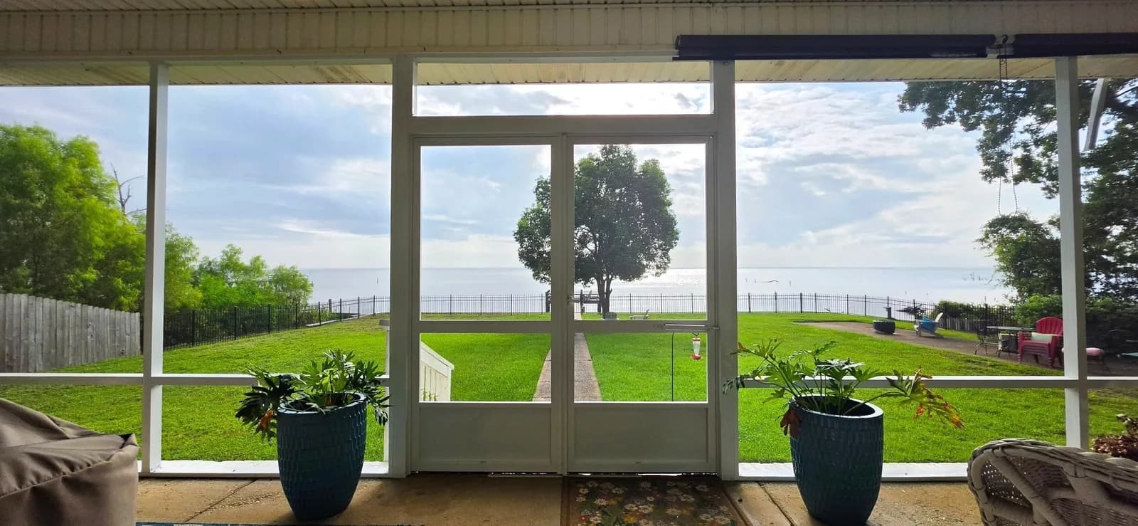 Screened porch with double doors and a panoramic Mobile Bay waterfront view beyond the mesh, Mobile AL.