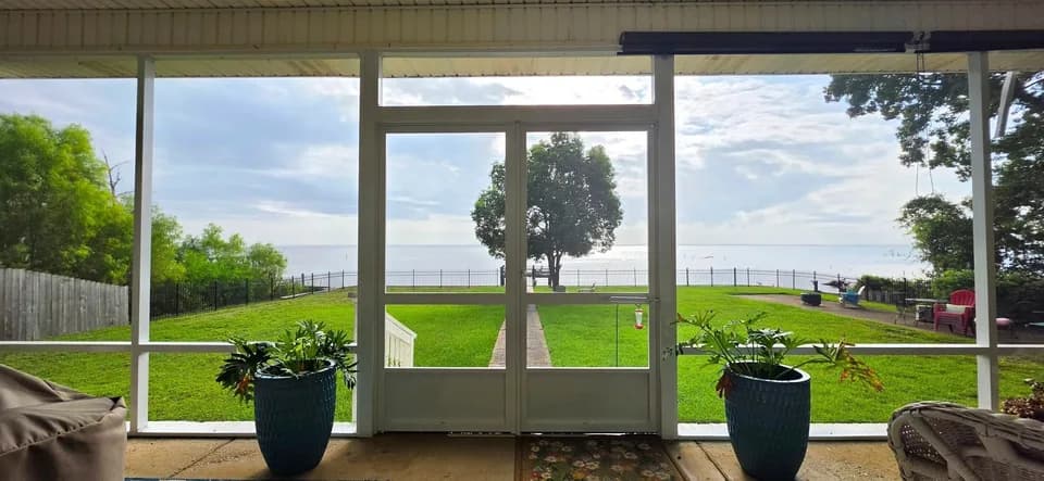 Screened porch with double doors and a panoramic Mobile Bay waterfront view beyond the mesh, Mobile AL.