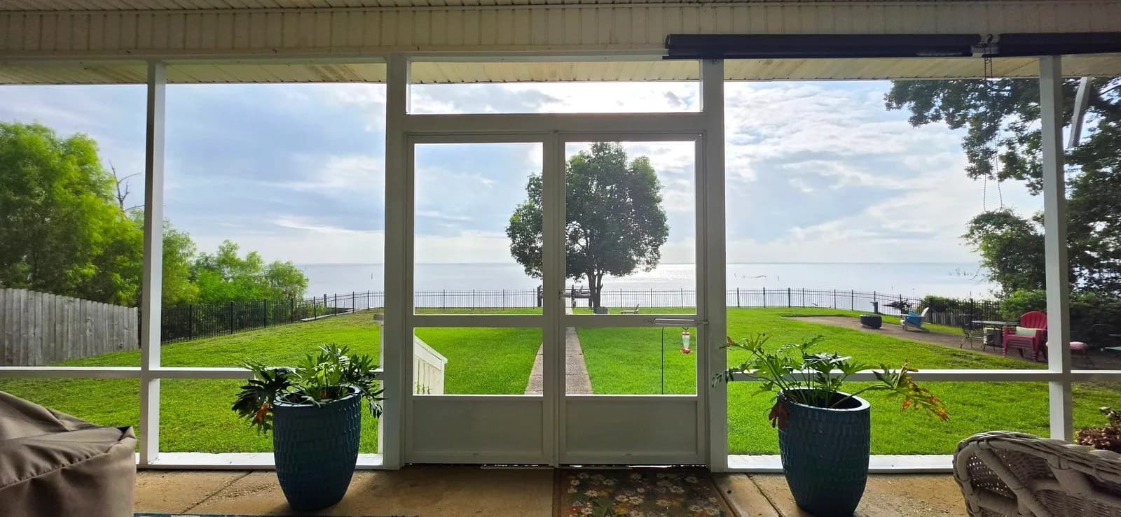 Screened porch with double doors and a panoramic Mobile Bay waterfront view beyond the mesh, Mobile AL.