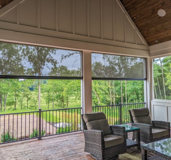 SunPro motorized solar screens lowered across a covered porch interior with wicker seating.