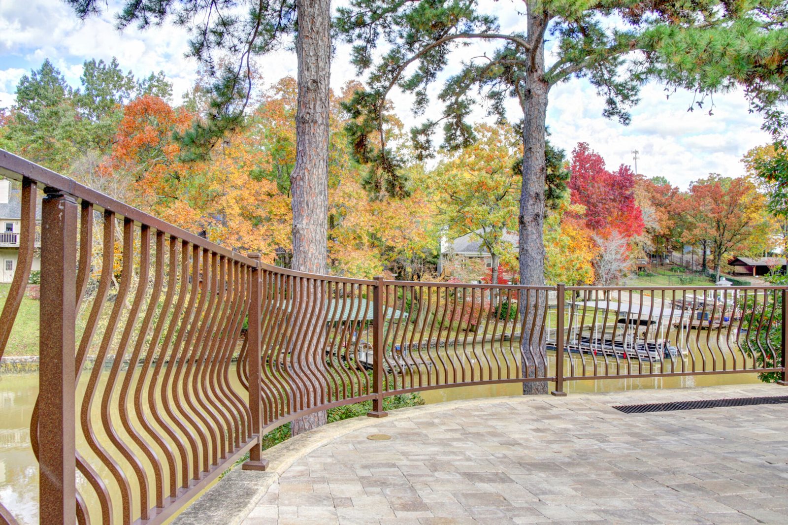 Curved brown Westbury aluminum railing along a waterfront patio with autumn trees beyond.